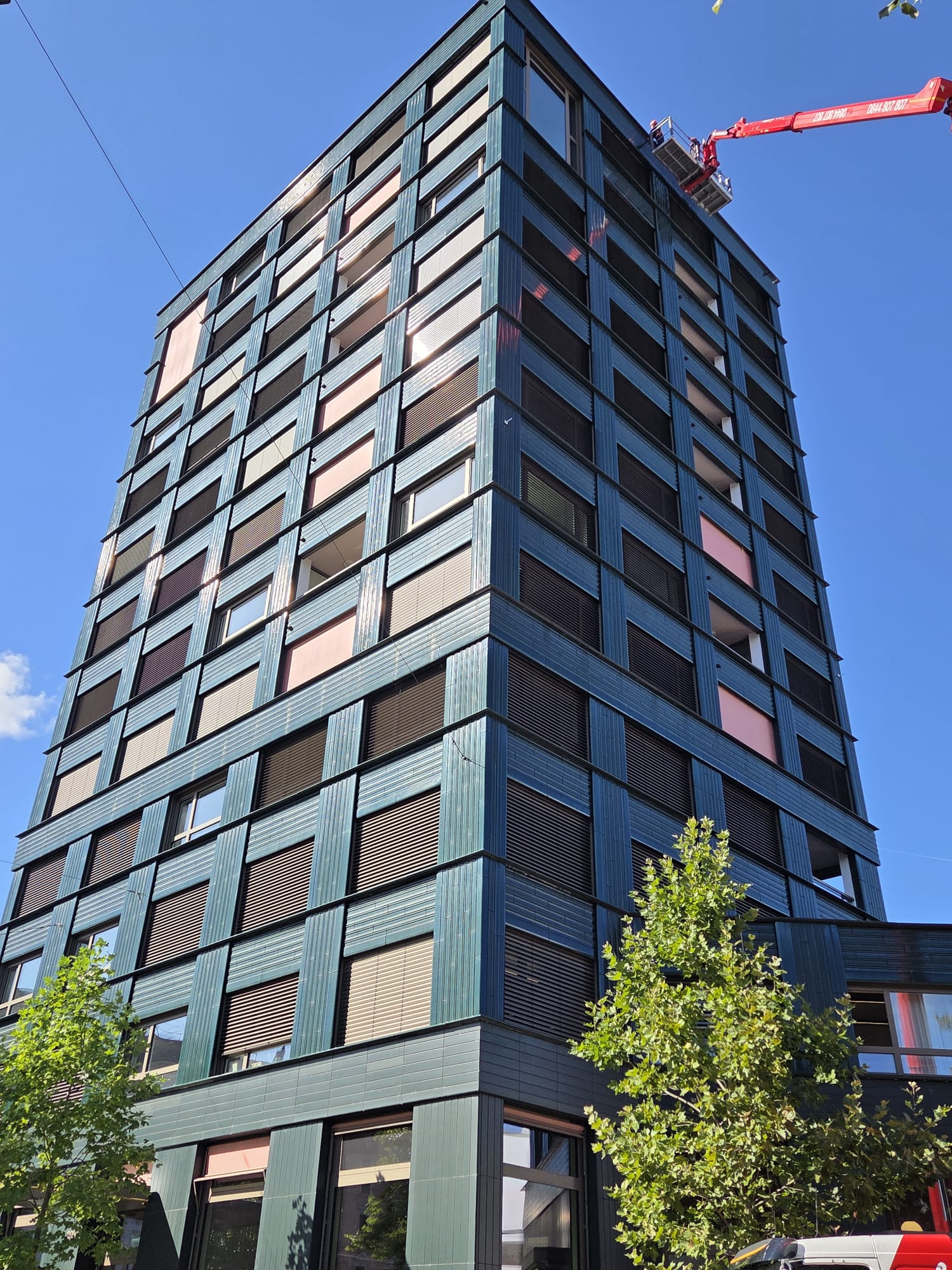 Wohn- und Geschäftshochhaus in Zürich mit Glasfassade und Fensterlamellen, oben die Arbeitsbühne
